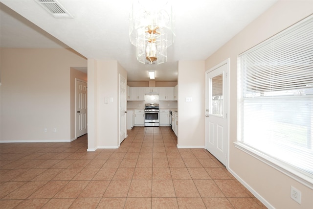 kitchen with light tile patterned floors, visible vents, stainless steel range, light countertops, and white cabinetry