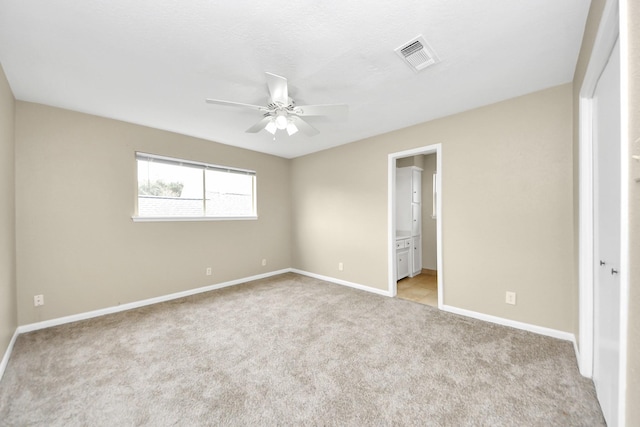 unfurnished bedroom with light carpet, baseboards, visible vents, a ceiling fan, and ensuite bathroom