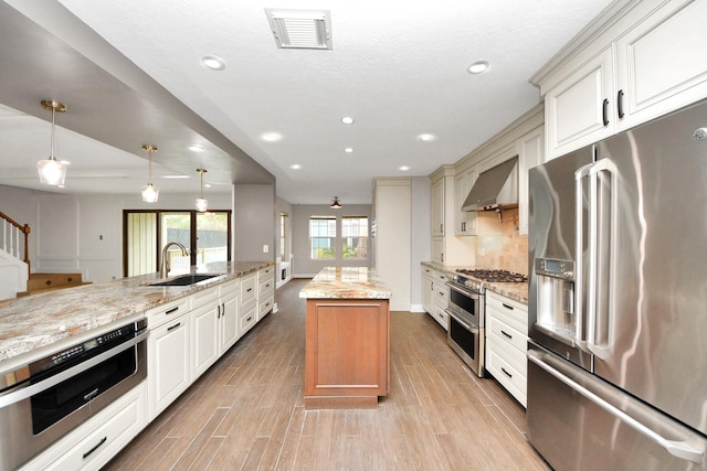 kitchen with visible vents, high end appliances, wall chimney exhaust hood, light wood-style floors, and a sink