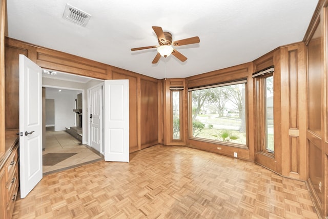 unfurnished room with a ceiling fan, visible vents, and wooden walls