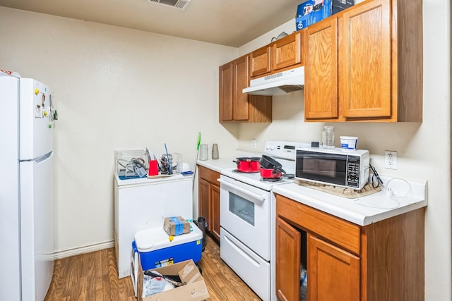 kitchen with under cabinet range hood, white appliances, light countertops, brown cabinets, and light wood finished floors