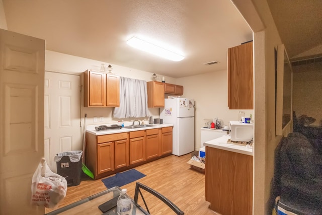 kitchen with brown cabinets, light wood finished floors, light countertops, freestanding refrigerator, and a sink