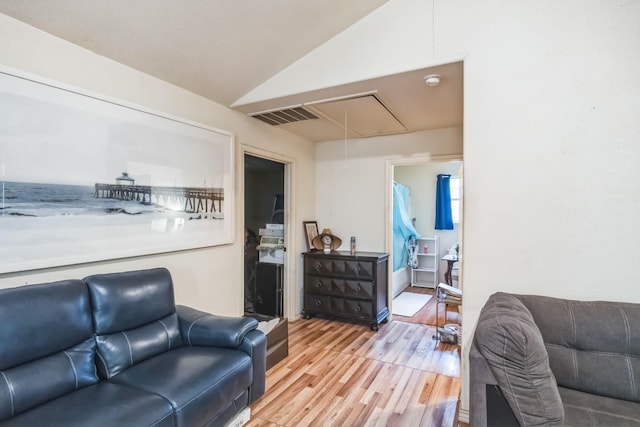 living room featuring attic access, visible vents, vaulted ceiling, and light wood finished floors