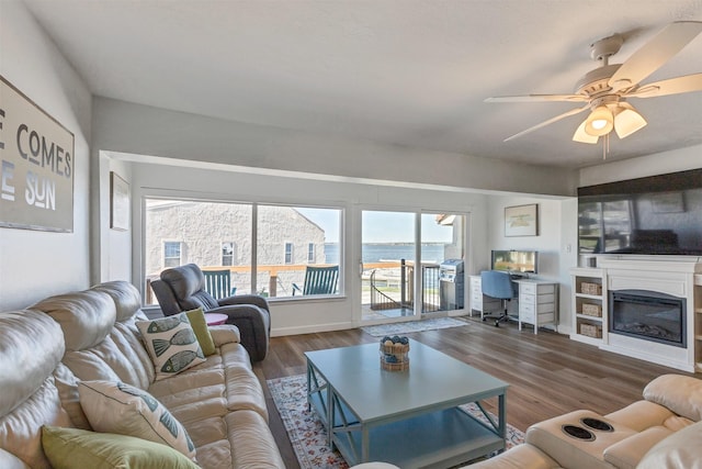 living room with a glass covered fireplace, wood finished floors, baseboards, and a ceiling fan