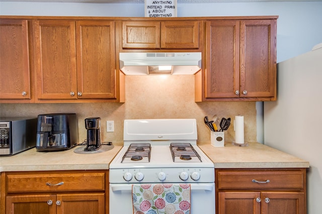 kitchen with white range with gas stovetop, stainless steel microwave, light countertops, and under cabinet range hood