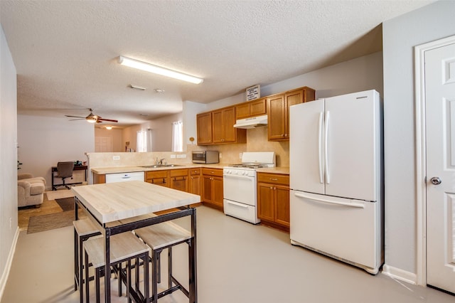 kitchen with white appliances, a peninsula, light countertops, under cabinet range hood, and a sink