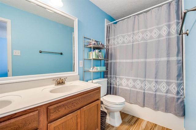 bathroom featuring double vanity, toilet, a sink, a textured ceiling, and wood finished floors