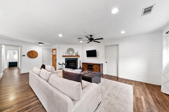 living area featuring a fireplace with raised hearth, a textured ceiling, dark wood finished floors, and visible vents