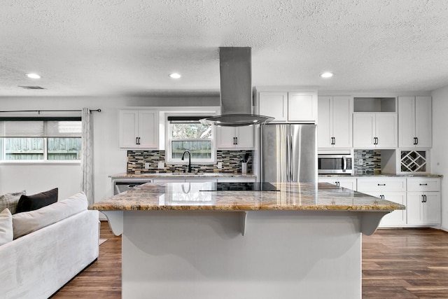 kitchen featuring stainless steel appliances, white cabinetry, a kitchen island, island range hood, and light stone countertops