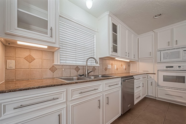 kitchen featuring glass insert cabinets, white cabinetry, a sink, dark tile patterned flooring, and white appliances