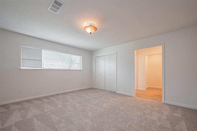 unfurnished bedroom featuring carpet, a closet, visible vents, a textured ceiling, and baseboards