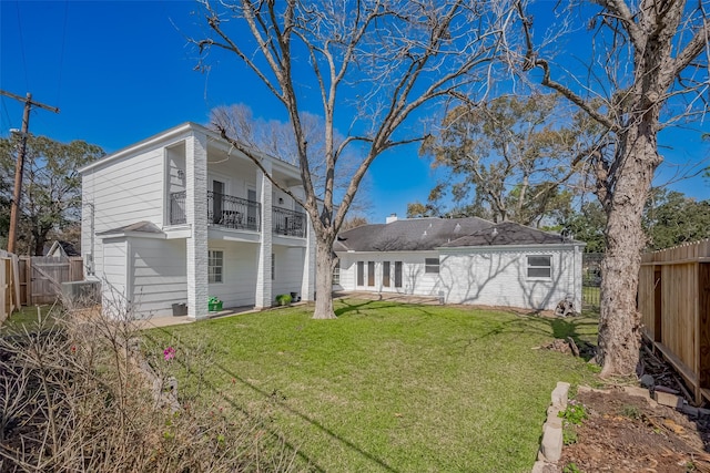 back of property with a balcony, a fenced backyard, and a yard