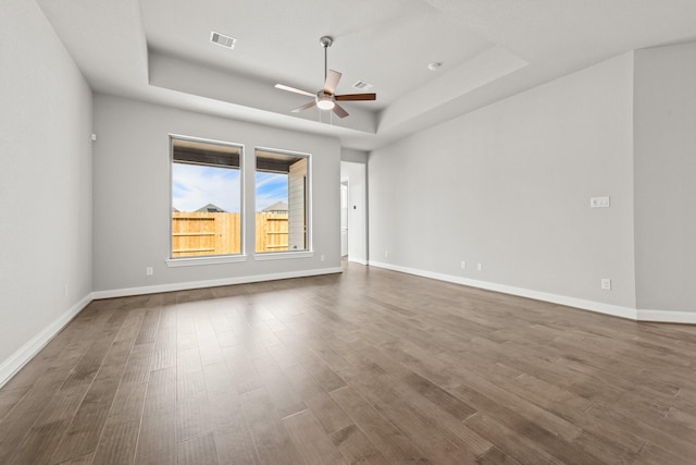 unfurnished room featuring a raised ceiling, visible vents, ceiling fan, wood finished floors, and baseboards