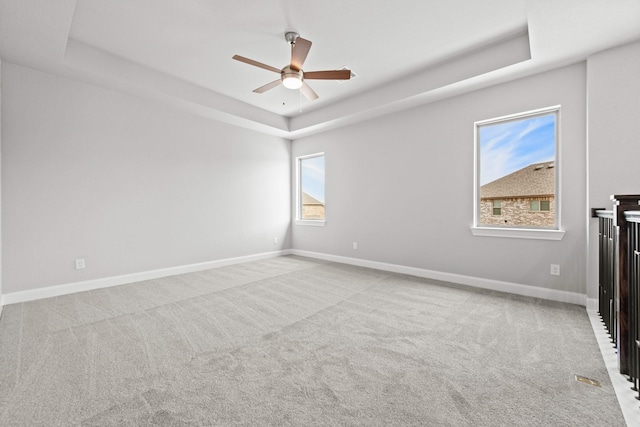 unfurnished room featuring baseboards, a raised ceiling, a ceiling fan, and light colored carpet