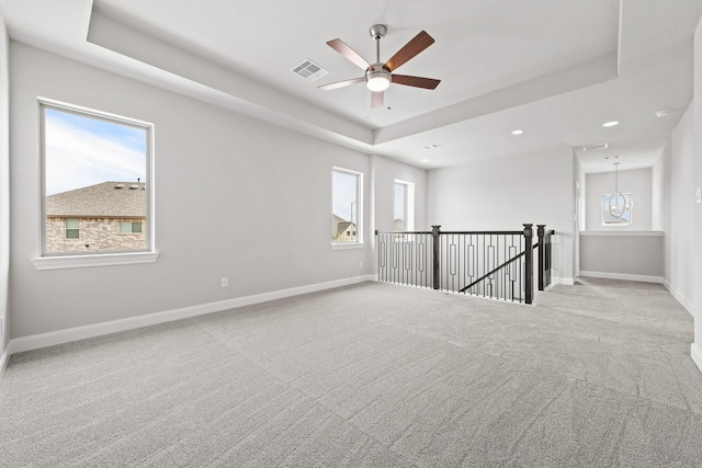 unfurnished room with visible vents, a tray ceiling, baseboards, and light colored carpet