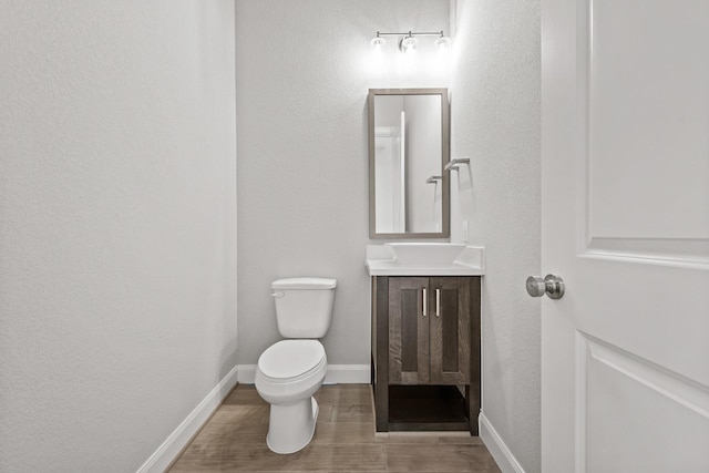 half bathroom featuring toilet, vanity, baseboards, and wood finished floors