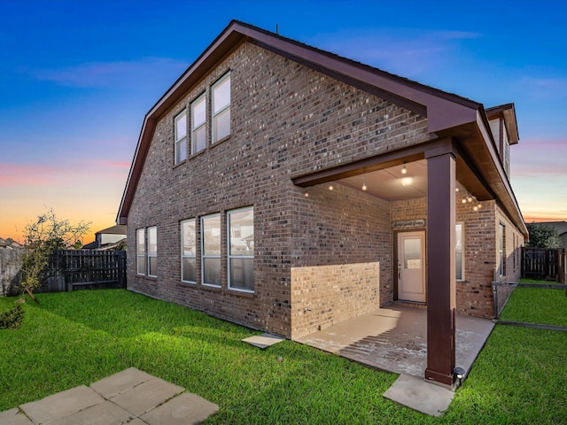 back of house at dusk with a patio area, brick siding, a lawn, and a fenced backyard