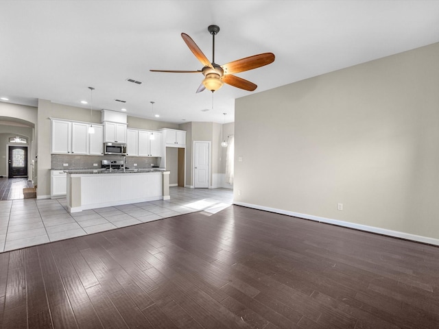 unfurnished living room featuring arched walkways, visible vents, light wood-style flooring, a ceiling fan, and baseboards