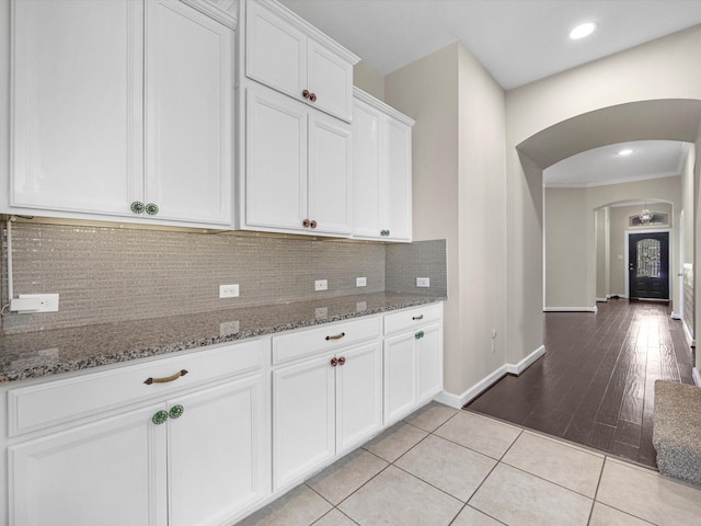 kitchen with light tile patterned floors, tasteful backsplash, arched walkways, white cabinets, and stone counters