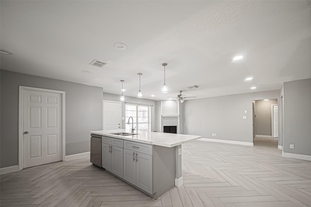 kitchen featuring a kitchen island with sink, gray cabinetry, stainless steel dishwasher, a fireplace, and a sink