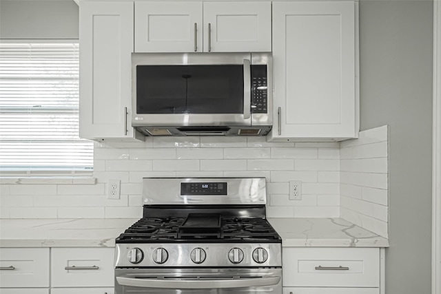 kitchen with stainless steel appliances, white cabinets, light stone counters, and tasteful backsplash