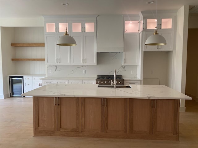 kitchen featuring beverage cooler, a center island with sink, custom exhaust hood, white cabinetry, and open shelves