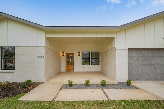 doorway to property with driveway, brick siding, board and batten siding, and an attached garage