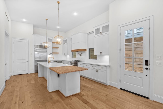 kitchen with premium appliances, a kitchen island with sink, white cabinetry, and light wood-style floors