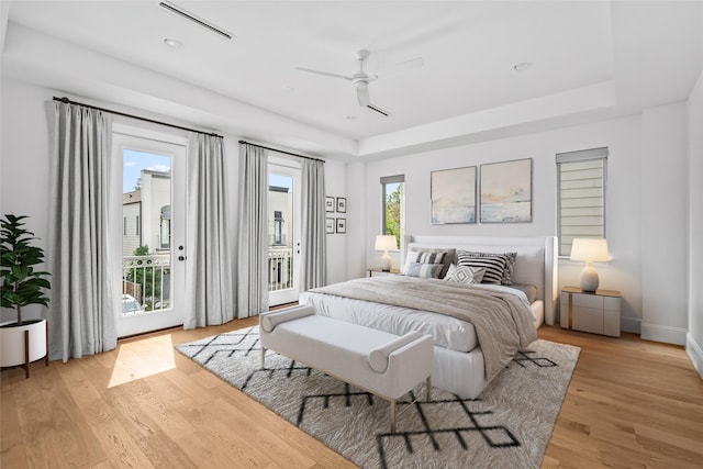 bedroom featuring access to exterior, light wood-type flooring, and a raised ceiling