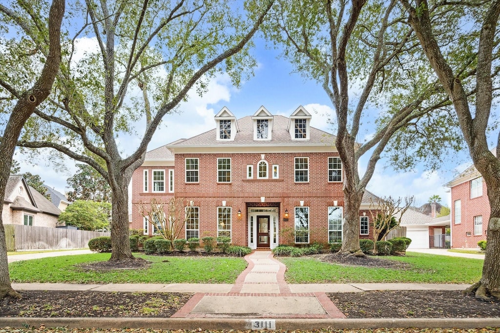 colonial-style house featuring a front yard, fence, and brick siding