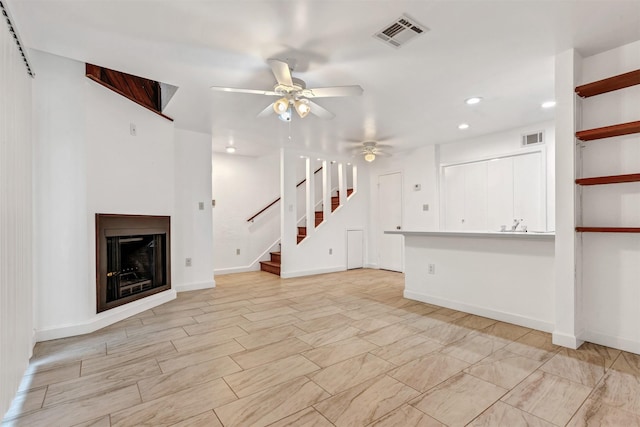 unfurnished living room with a ceiling fan, visible vents, a fireplace, and stairs