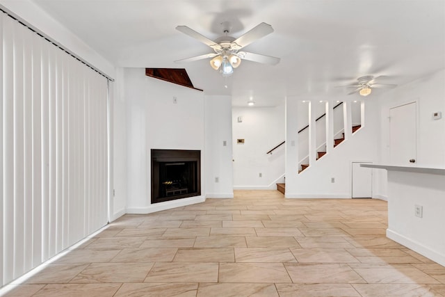 unfurnished living room with a ceiling fan, a fireplace, stairway, and baseboards