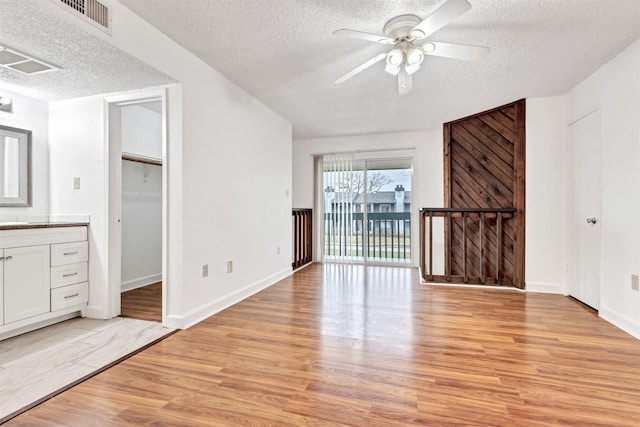 interior space featuring light wood-style floors, ceiling fan, visible vents, and a textured ceiling