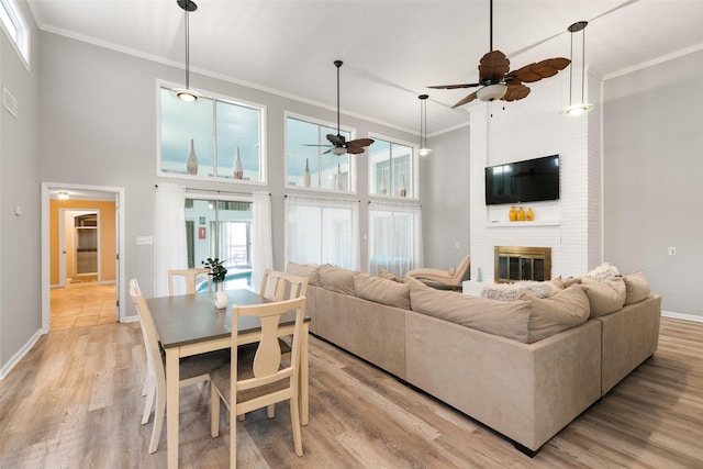 living room with crown molding, light wood-style flooring, a towering ceiling, a brick fireplace, and baseboards