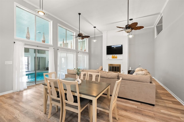 dining area with light wood-style floors, a brick fireplace, and crown molding