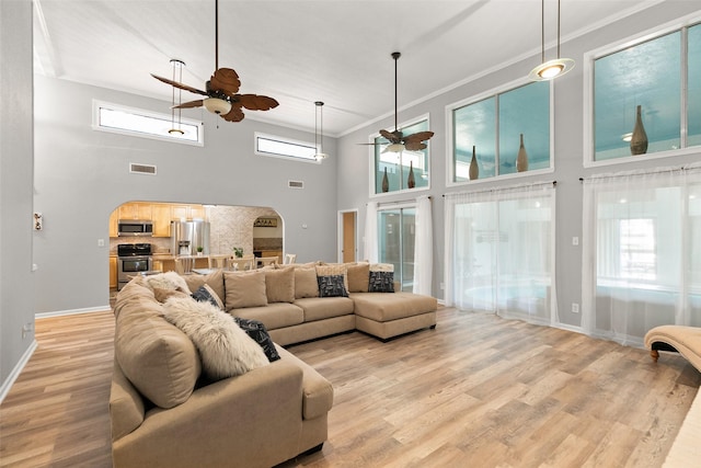 living room with crown molding, light wood finished floors, visible vents, a ceiling fan, and a healthy amount of sunlight