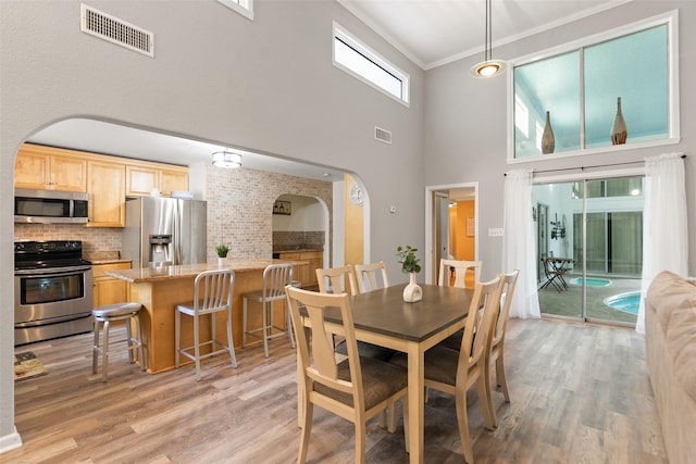 dining area with arched walkways, crown molding, visible vents, and light wood-style floors