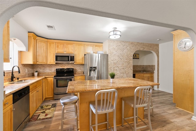 kitchen with arched walkways, stainless steel appliances, a sink, light wood-style floors, and decorative backsplash