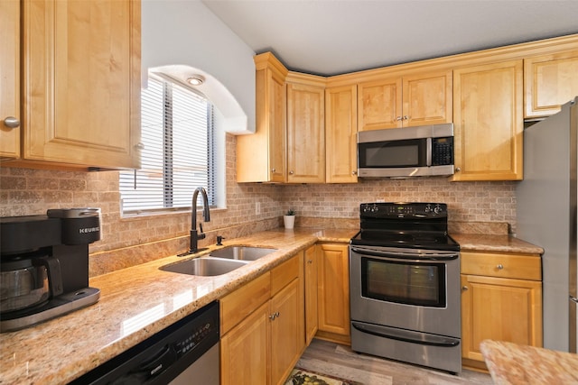 kitchen with light brown cabinets, stainless steel appliances, a sink, light stone countertops, and tasteful backsplash