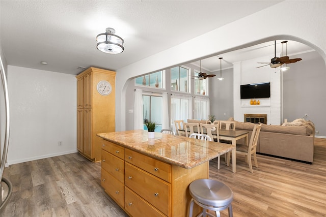 kitchen with arched walkways, light wood finished floors, a fireplace, and a kitchen island