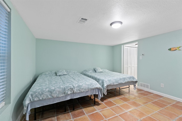 bedroom with tile patterned flooring, visible vents, a textured ceiling, and baseboards