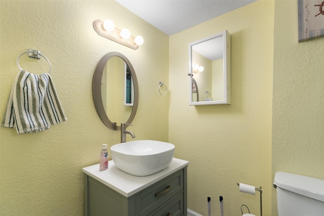 bathroom featuring toilet, a textured wall, a textured ceiling, and vanity