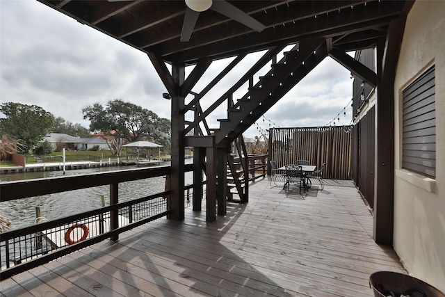 wooden terrace with outdoor dining space, stairway, a water view, and a ceiling fan