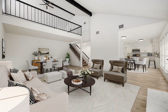 living room with visible vents, light wood-style flooring, ceiling fan, stairs, and beam ceiling