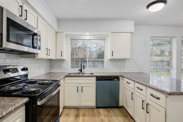 kitchen featuring light wood-style flooring, a peninsula, a sink, a healthy amount of sunlight, and appliances with stainless steel finishes