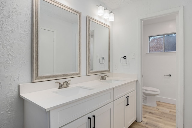 full bath featuring double vanity, a sink, toilet, and wood finished floors