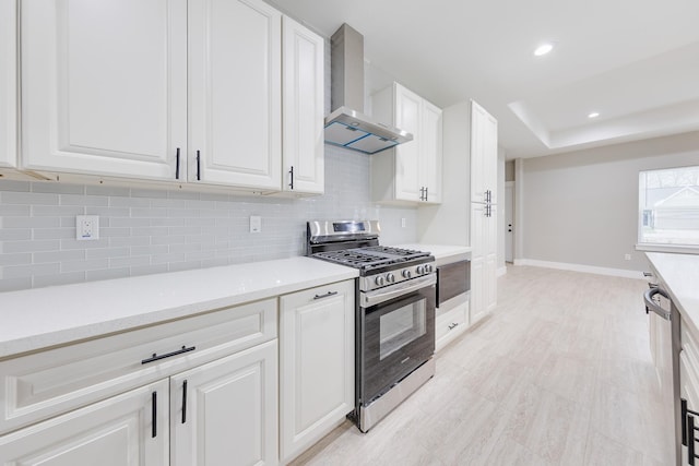 kitchen featuring wall chimney range hood, white cabinetry, appliances with stainless steel finishes, and light countertops