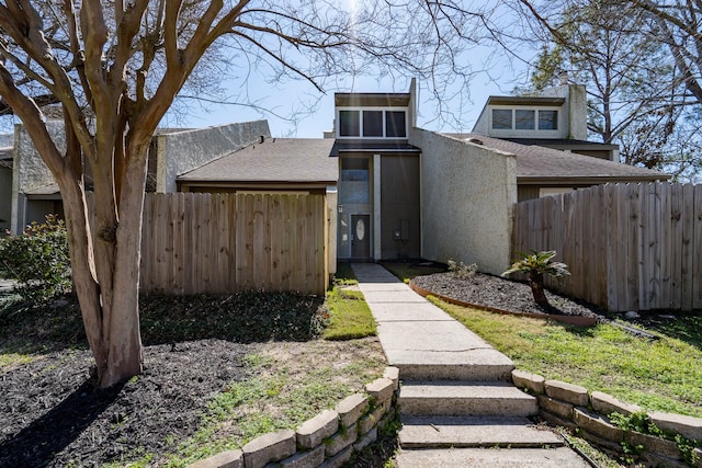 view of front of home featuring roof with shingles, fence, and stucco siding