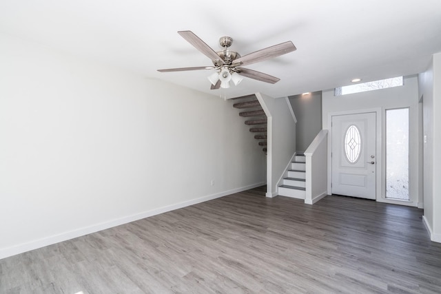 foyer entrance with a ceiling fan, baseboards, stairway, and wood finished floors