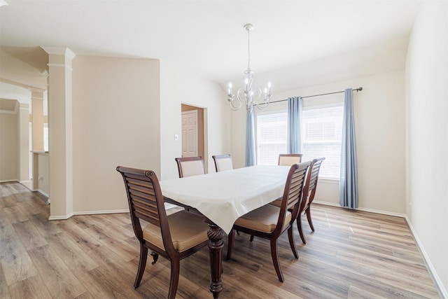 dining room featuring light wood finished floors, baseboards, a chandelier, and ornate columns